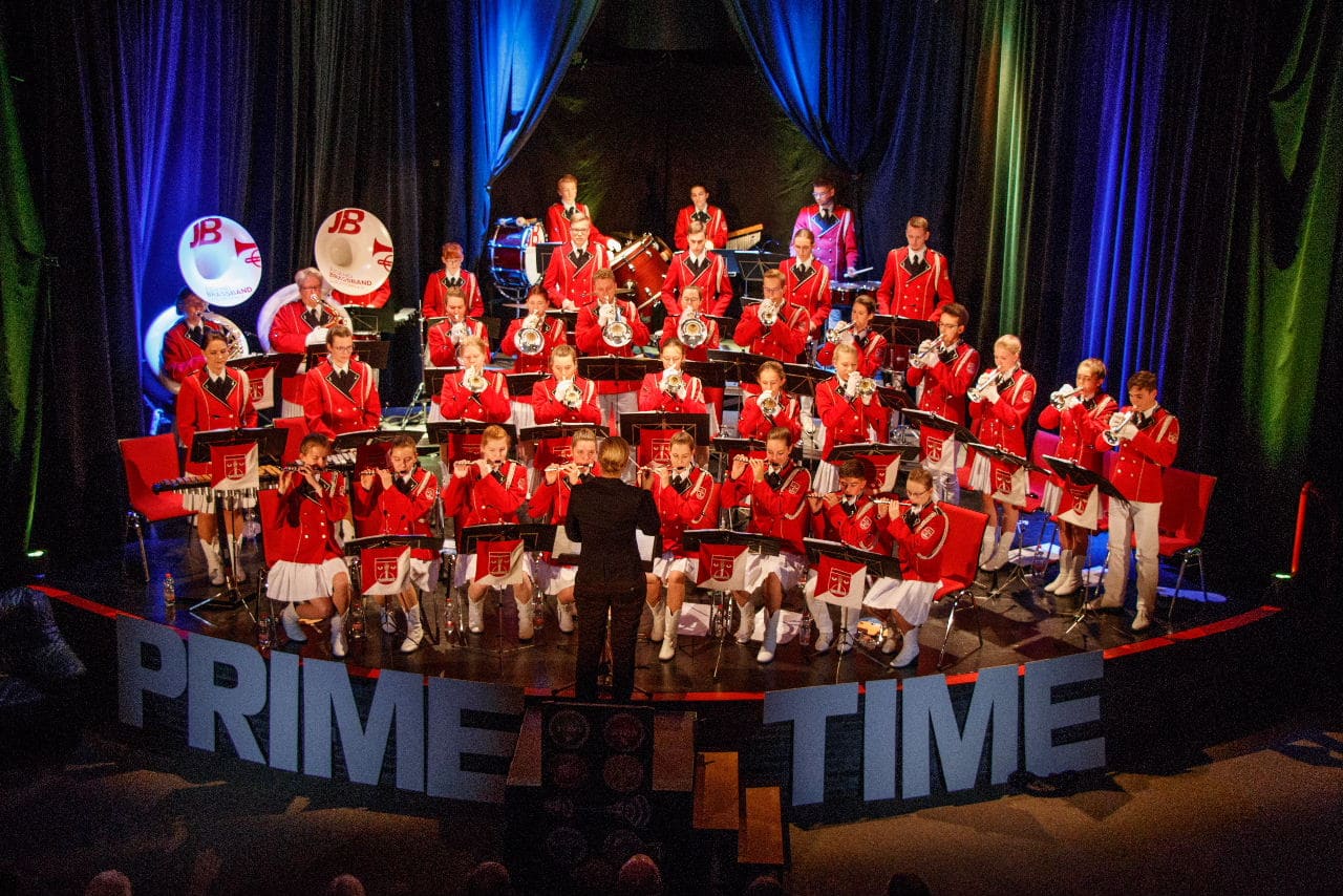 Die Band in roten Uniformen auf der Bühne, vorn die Dirigentin, an den Notenpulten die roten Behänge